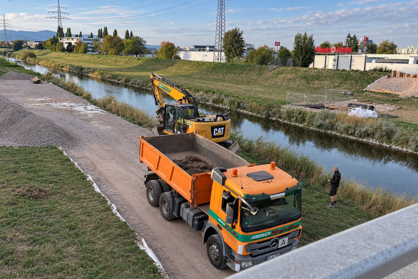 Lkw und Bagger der Schille GmbH bei Erdarbeiten am Flussufer in Offenburg